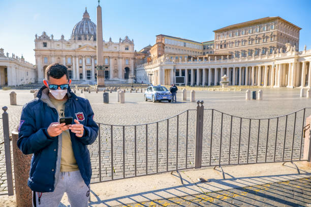 A tourist visits St. Peter's Square closed and deserted due to the Covid-19 lockdown Vatican, Italy, March 11 -- A tourist protected by a medical mask in the square of St. Peter's Basilica closed to visitors and completely deserted, controlled by an Italian police patrol. In the background on the right the Apostolic Palace, seat of the Catholic Pontiff. church of san pietro photos stock pictures, royalty-free photos & images