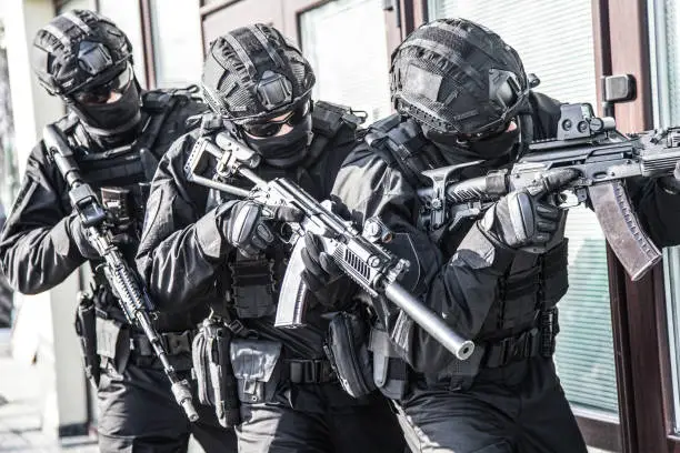 Police counter terrorist tactical unit, special reaction team in black blank uniforms with hidden identity, armed with assault rifles, moving in stack formation during terrorism response operation