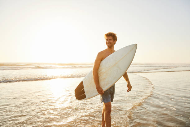 istock Smiling young man walking in the ocean with a surfboard 1212005395