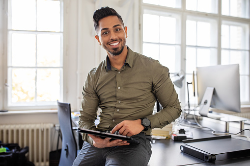 Portrait of young businessman standing at his desk with a digital tablet. Confident businessman in a modern office.