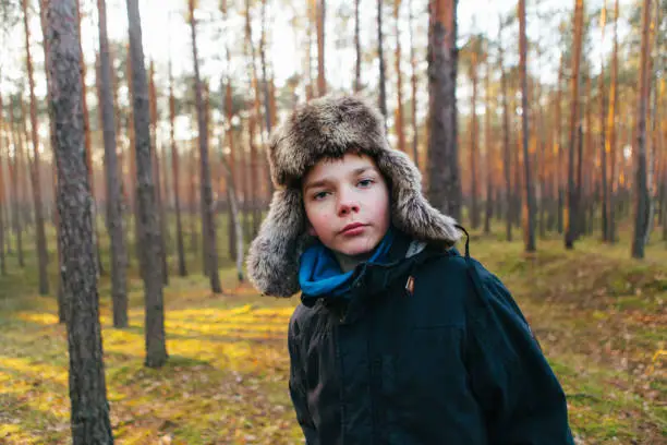 December 1, 2018 - Kampinos, Poland: mischievous smart boy in warm clothing posing for a portrait in a sunlit pine forest