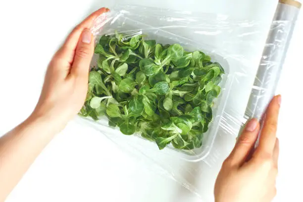 Woman using food film for food storage on a white table. Roll of transparent polyethylene food film.