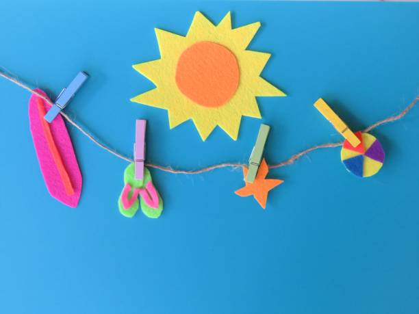 summer sun beach items clothespinned to clothesline. Copy space. Felt craft. Blue background. summer sun beach items-surfboard, sandals, starfish, beach ball-clothes pinned to line,.Copy space; blue background; felt craft. christine kohler stock pictures, royalty-free photos & images