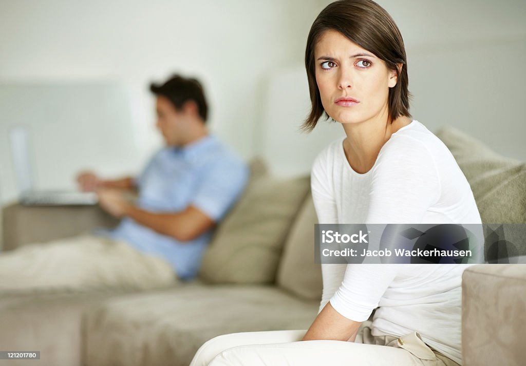 Unhappy young female sitting with her husband in the background  Negative Emotion Stock Photo