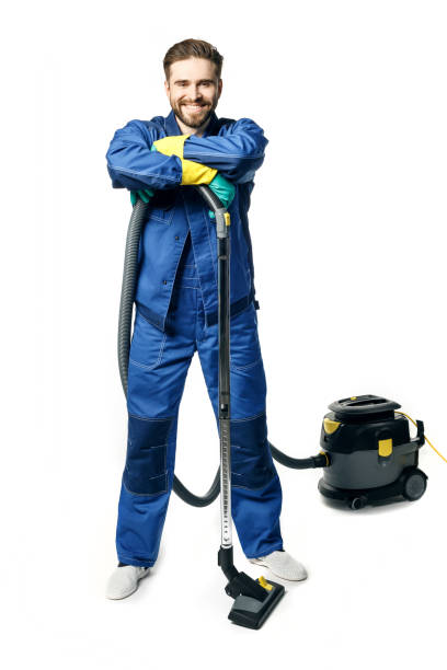 istock Young handsome man with a beard in a blue working uniform for cleaning rooms smiling and vacuuming isolated on white background. 1212017999