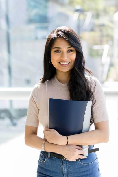 istock Female student with long hair carries notebook; smiles for camera 1212021317