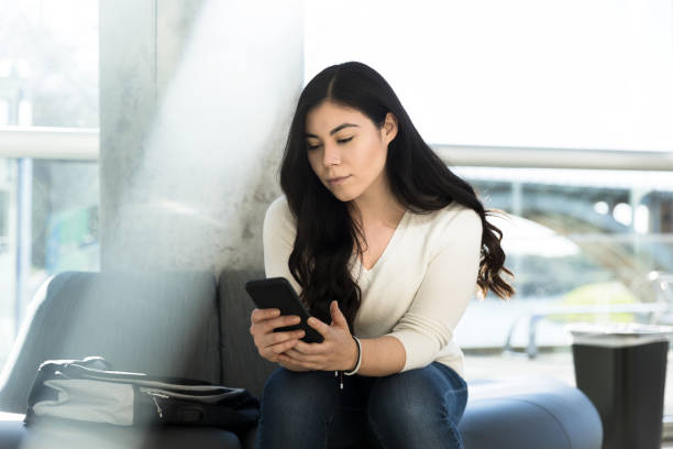 istock Seated female student with back pack texts messages on phone 1212021371
