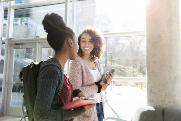 Attentive female student talks with friend While walking to class, a female college student smiles while talking to her friend. community college stock pictures, royalty-free photos & images