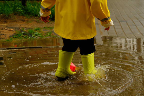 child jumps in a puddle arranges a storm for a small plastic boat. legs in yellow rubber boots