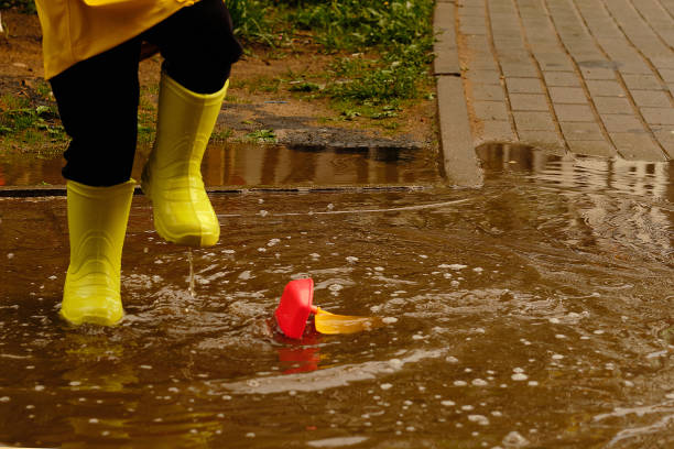 little boy plays with a plastic boat in a puddle on a rainy autumn day