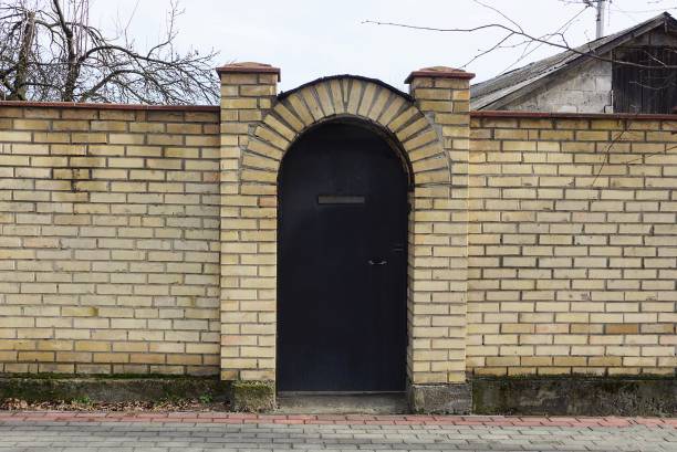 one black iron closed door on a brown brick fence on a rural street