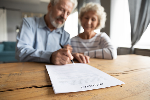 Close up of happy mature 60s couple spouses clients close deal sign insurance contract with specialist, smiling middle-aged old husband and wife put signature make agreement, elderly care concept