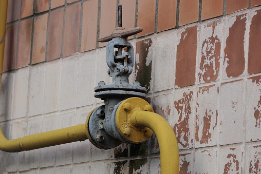 gray iron valve with a yellow gas pipe against a brown wall