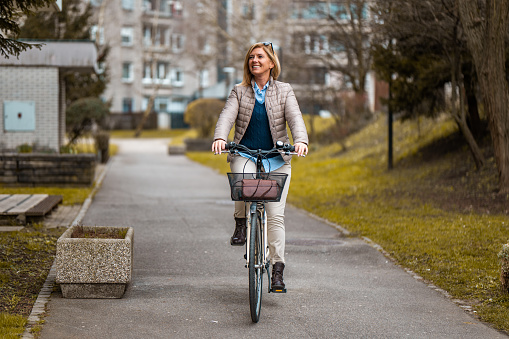 Adult caucasian woman in a smart casual clothes riding a bicycle in a residential district.