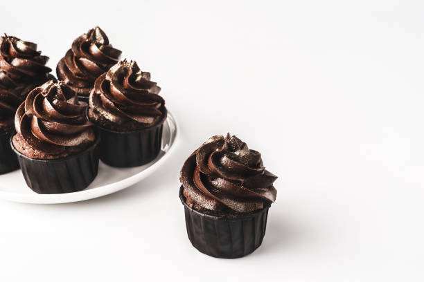 istock Chocolate cupcakes with chocolate icing and sprinkled gold sparkles on white porcelain plate on isolated white background. Mockup for your design. Close-up. Copy space. 1212049689