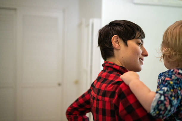 This is a photograph of a Caucasian gender neutral person in their 30s with short hair bonding with their baby relative as they spend time together indoors.
