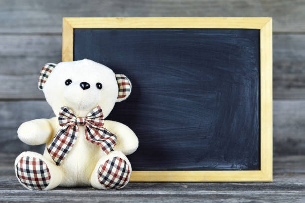 Teddy bear with blank blackboard on wooden background
