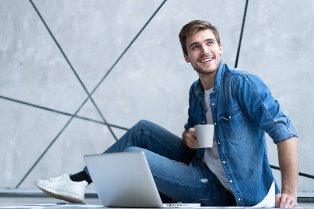 istock Man working at home. Handsome young man sitting on the floor and examining document while laptop and documents laying near him. 1212055570