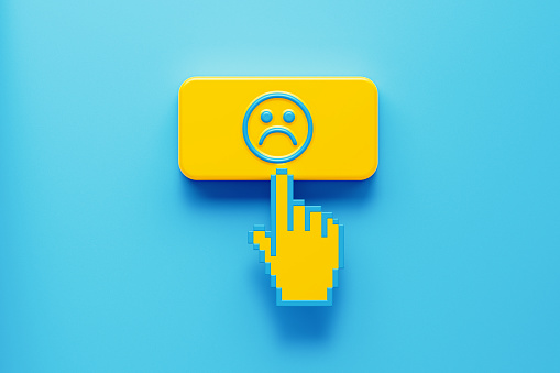 Hand shaped computer cursor clicking on a yellow computer button on blue background. There is sad face icon on push button. Horizontal composition with copy space. Rating concept.