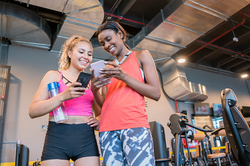 Women, youth, friends, of Latin race, smiling and talking, while they look at their cell phones, after finishing their exercise routine