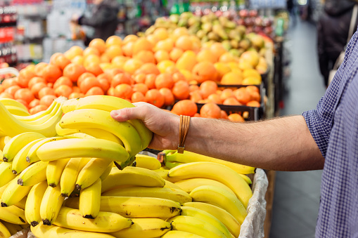mans hand take bananas from shelf of store. healthy food. shopping concept.