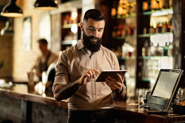 barista souriant utilisant la tablette numérique tout en travaillant dans un bar. - point de vente photos et images de collection