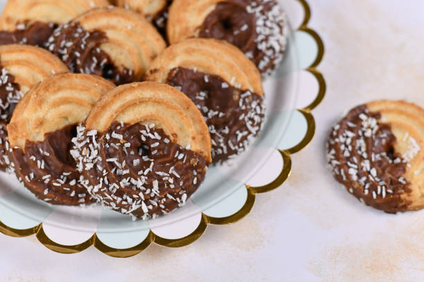 istock Round ring shaped spritz biscuits with half side glazed with chocolate and topped with coconut sprinkles on plate 1212064230