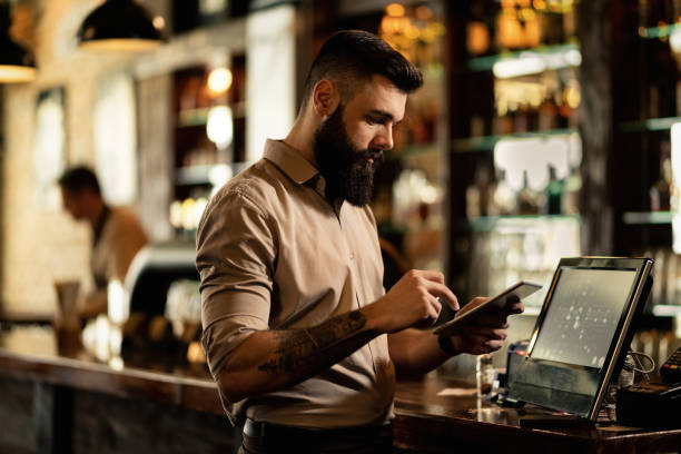 istock Young barista using touchpad while standing at cash register in a bar. 1212064301