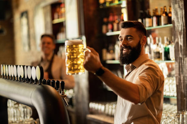 バーカウンターでドラフトビールのグラスを持つハッピーバリスタ。 - beer bar counter bar beer glass ストックフォトと画像