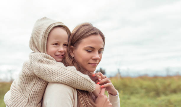 little boy hugs woman mom, autumn day on nature in field, warm beige sweater with hood. Emotions of care nurturing love and support. Free space for copy text. Happy smiling rejoices. stock photo