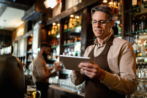 istock Smiling mid adult waiter using touchpad while working in a bar. 1212065264