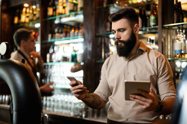 istock Young barista texting on the phone while using touchpad in a pub. 1212065394