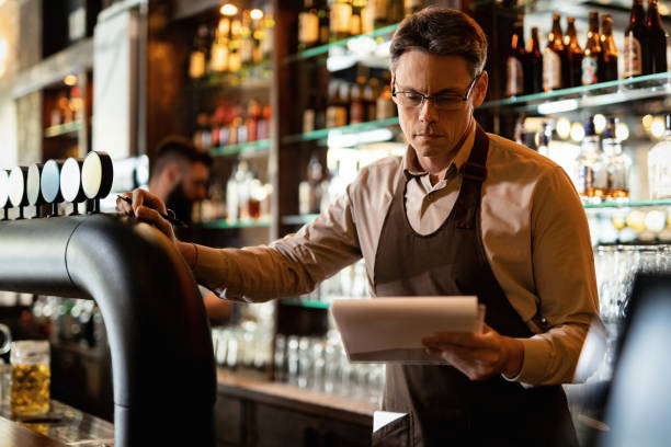 istock Barista reading inventory list while working behind bar counter. 1212065416