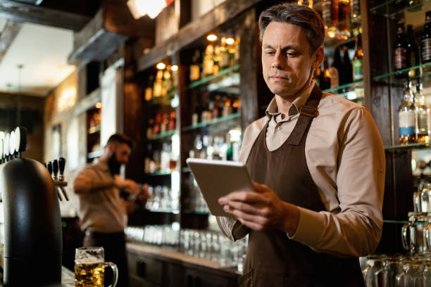 istock Smiling barista working on digital tablet in a pub. 1212065476