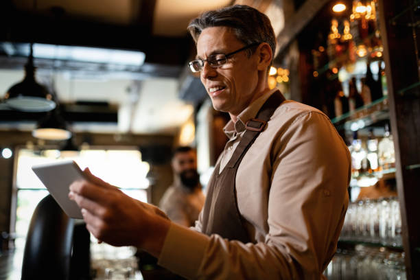 istock Happy mid adult waiter using digital tablet while working in a pub. 1212065576