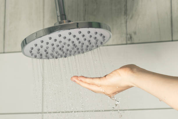 mano femenina tocando agua que vierte desde un cabezal de ducha de lluvia, comprobando la temperatura del agua - fountain house residential structure home interior fotografías e imágenes de stock