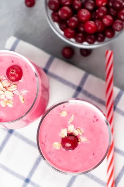 dvě sklenice s čerstvě domácím smoothie jogurtu, ovesných vlčích a brusinek na šedém stole. koncept zdravého stravování, vertikální plochá - jogurt fotky - stock snímky, obrázky a fotky