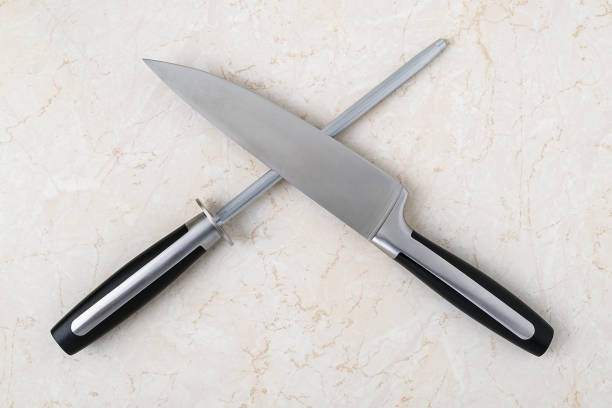 Professional chef knife and a sharpening steel lying crosswise on a kitchen table. Modern kitchen utensils made of high carbon molybdenum vanadium steel. Professional chef knife and a sharpening steel lying crosswise on a kitchen table. Modern kitchen utensils made of high carbon molybdenum vanadium steel. Top view. sharpening photos stock pictures, royalty-free photos & images