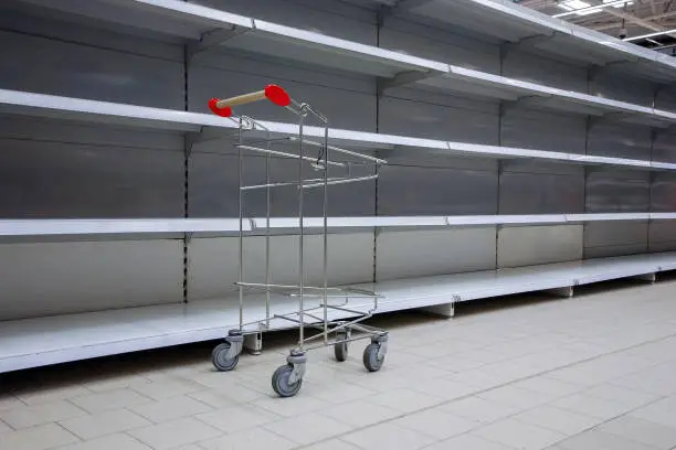 empty shelves and shopping cart in supermarket, all sold out due to panic caused by virus outbreak