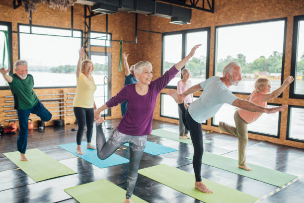 gruppe von senioren üben balance auf dem yoga-kurs - group of people aging process home interior indoors stock-fotos und bilder