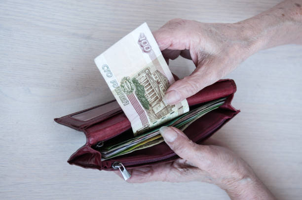 istock Old women's hands pull out a hundred rubles from a purse on the table. The concept of pensions 1212082736
