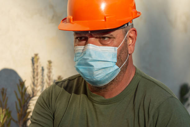 Hard hat worker wearing surgical mask to avoid spreading or being infected with airborne viruses