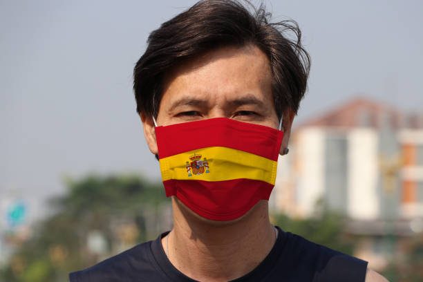 Spain flag on hygienic mask. Masked Asian man prevent germs. concept of Tiny Particle protection or virus corona. stock photo