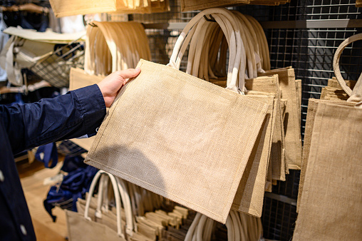 Male hand customer choosing brown jute handbag in craft shop. Reusable and Eco-friendly material bag for shopping. Buying concept