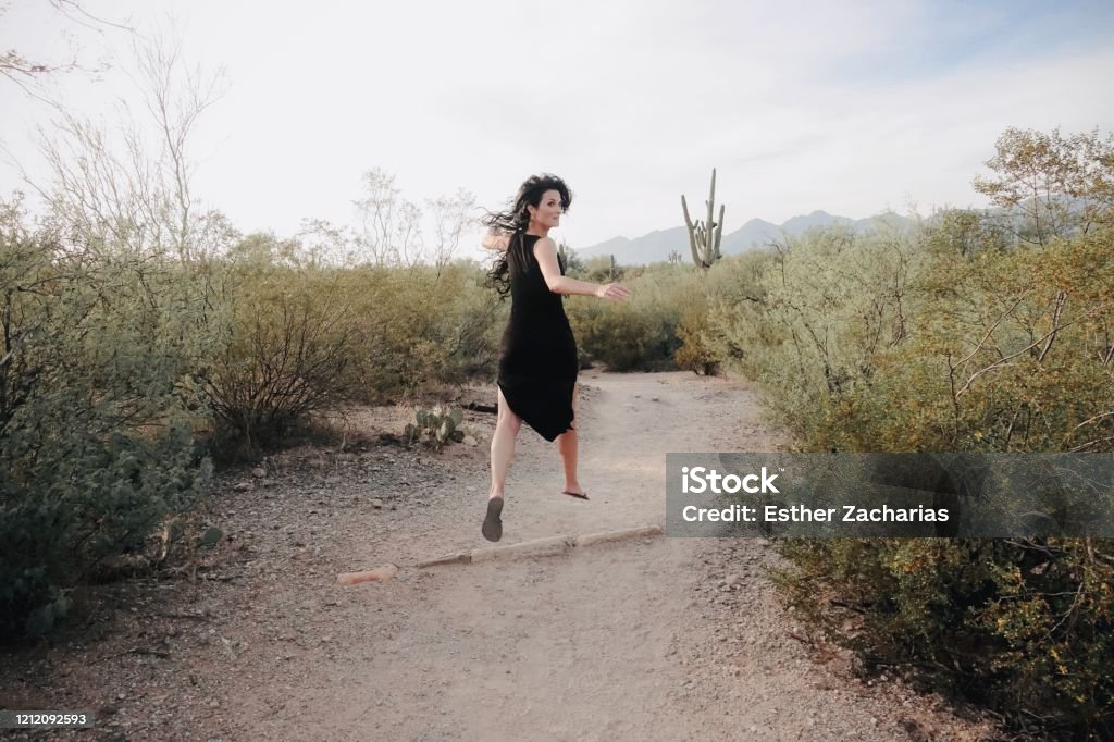Woman jumping with long hair in black dress in the desert Jumping Stock Photo