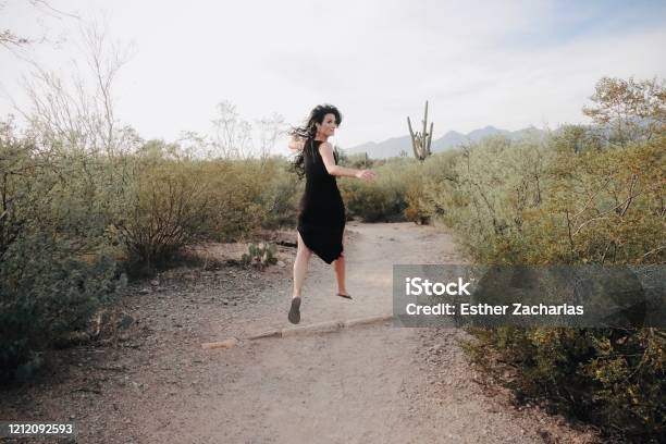 Woman Jumping With Long Hair In Black Dress In The Desert Stock Photo - Download Image Now