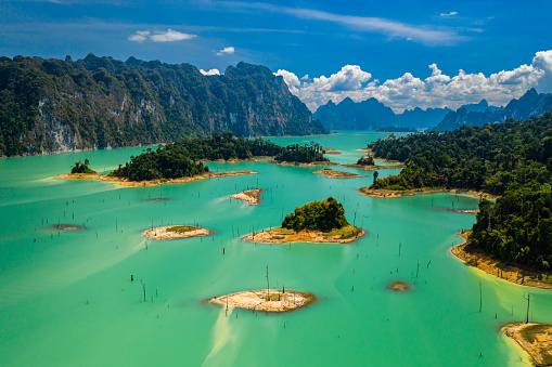 Aerial drone view looking down onto tiny, jungle covered islands in a huge lake surrounded by limestone cliffs. (Cheow Lan Lake, Khao Sok)