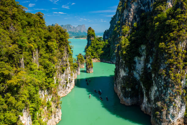 Aerial drone view of longtail boats around spectacular limestone fingers and karsts on a huge lake surrounded by jungle Aerial drone view of longtail boats around spectacular limestone fingers and karsts on a huge lake surrounded by jungle kao sok national park stock pictures, royalty-free photos & images