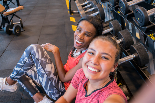 Female friends of Latin ethnicity between the ages of 20-30 years of different races are taking a selfie in the weight area of the gym