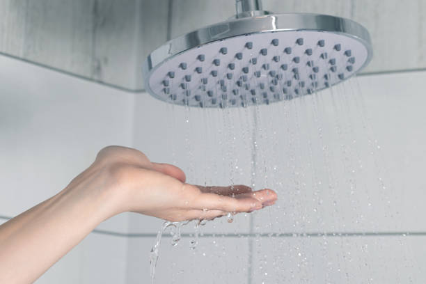 mano femenina tocando agua que vierte desde un cabezal de ducha de lluvia, comprobando la temperatura del agua - fountain house residential structure home interior fotografías e imágenes de stock